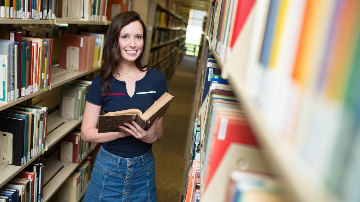 Young woman holds a book while standing among the stacks of the Coates 图书馆